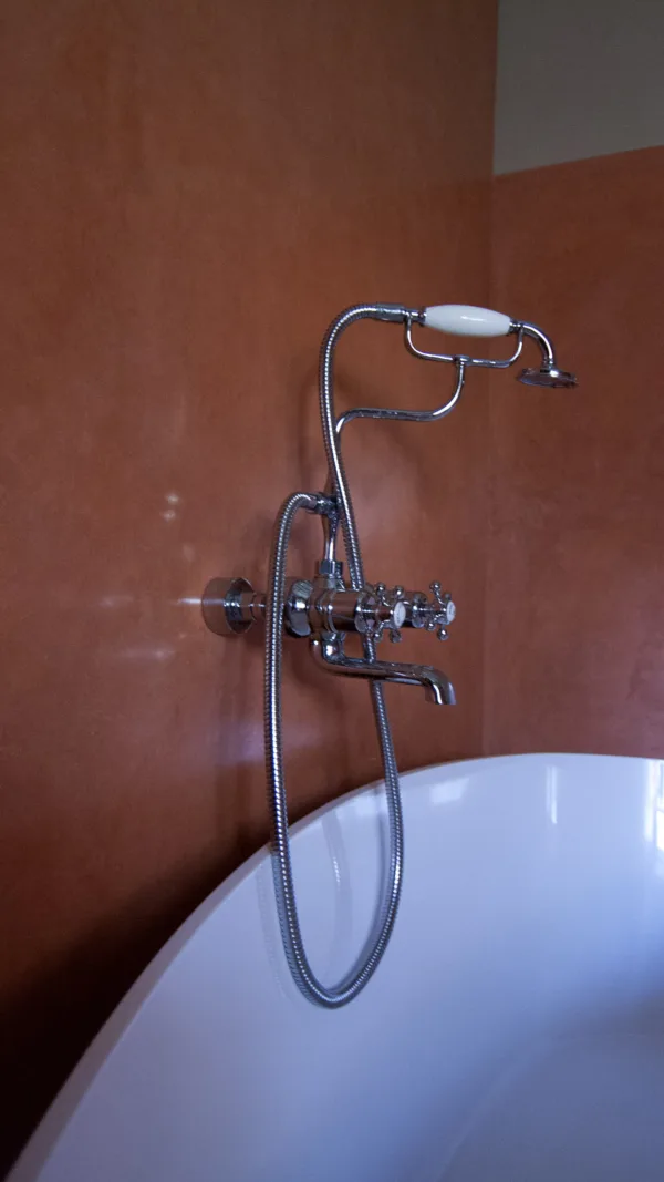 The soft curves of a freestanding bathtub are mirrored in the lustrous surface of Artisan Stucco Mortars Coral Red waterproof plaster.