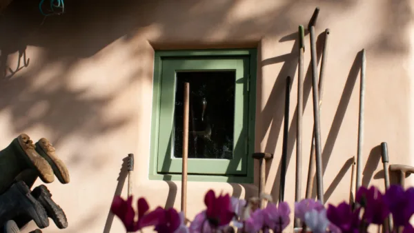 A warm Alhambra-toned Artisan Stucco floated finish on a natural lime cottage façade, softened by the play of sunlight and garden life. The casually leaning garden tools hint at the strength and resilience of the traditional lime plaster.